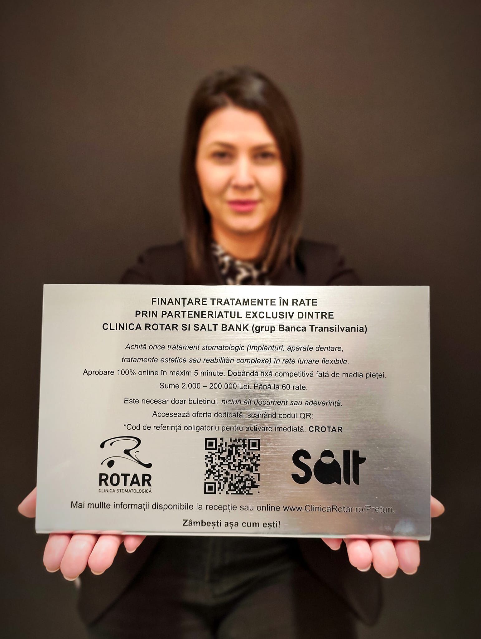 Patient holding Clinica Rotar financing plaque with Salt Bank QR code for instant loan approval